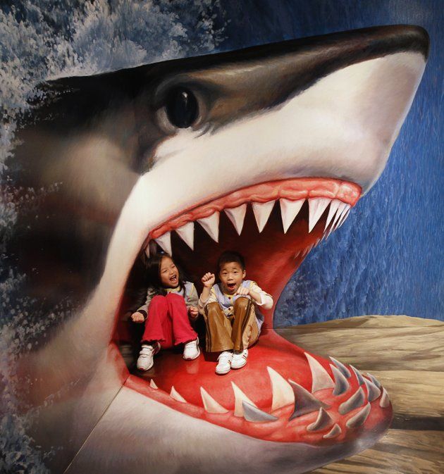 two children are sitting on top of a fake shark's mouth while another child looks on