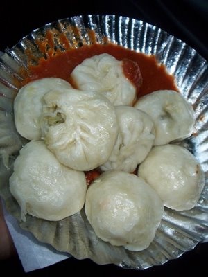 some dumplings are sitting in a tin foil plate with sauce on it and being held by someone's hand