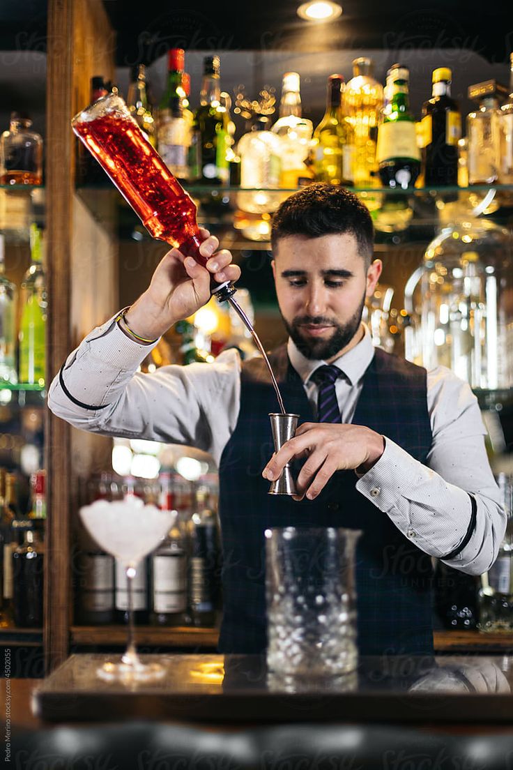 a man in a vest and tie holding a cocktail glass with a red liquid pouring into it