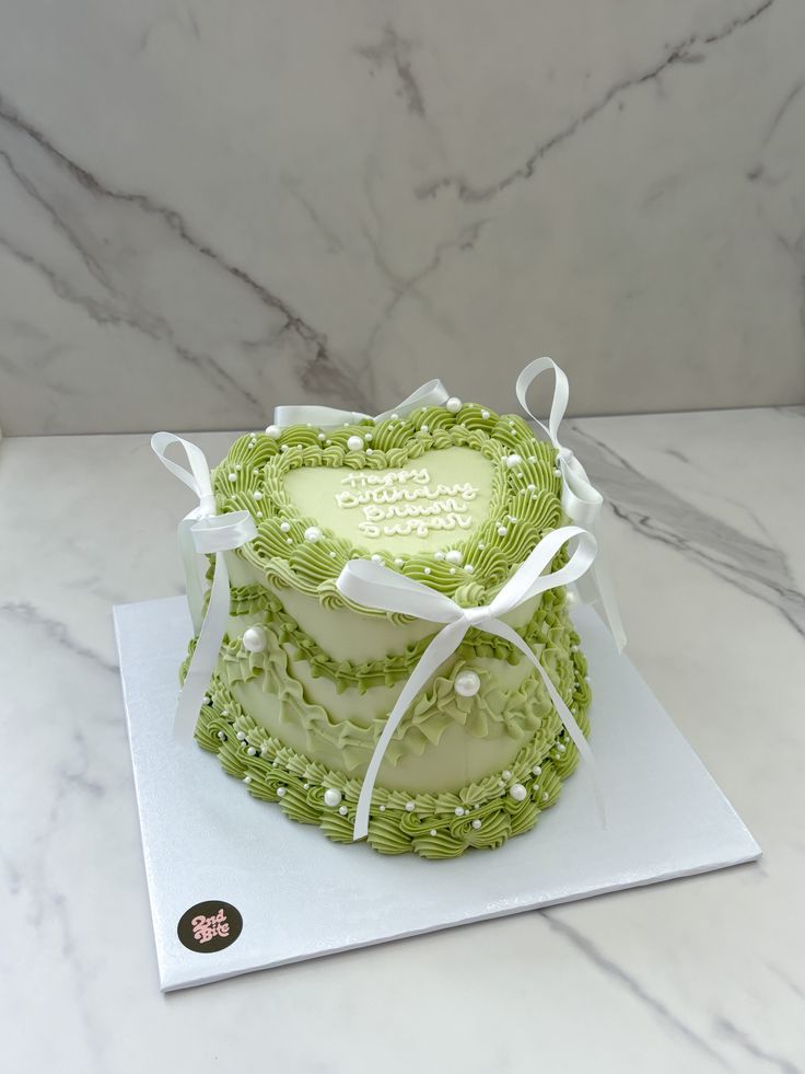 a heart shaped cake sitting on top of a white tablecloth covered counter next to a marble wall