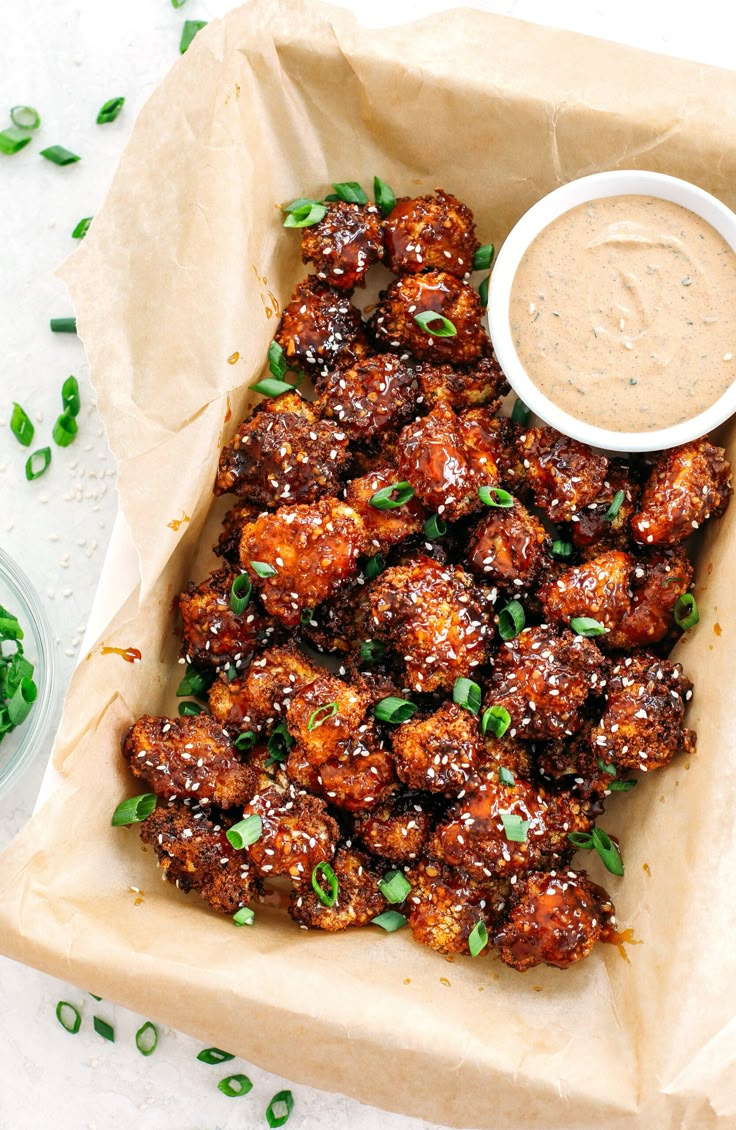 a plate with some food on it next to a bowl of sauce and green onions