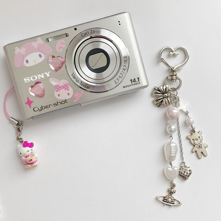 a silver camera sitting next to a keychain with hello kitty charms on it