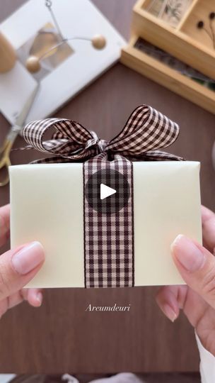 a person holding up a white box with a brown ribbon on it and a bow