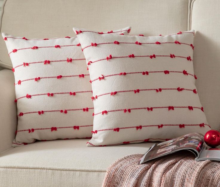 two pillows sitting on top of a couch next to a pillow with red stringing