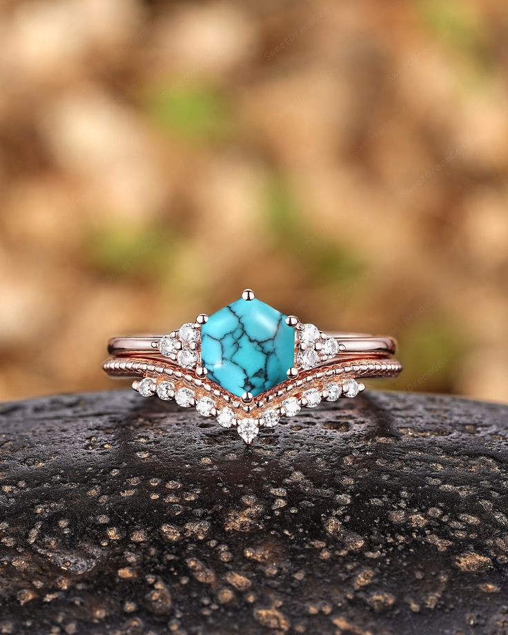 a turquoise stone and diamond ring sitting on top of a rock in front of some rocks