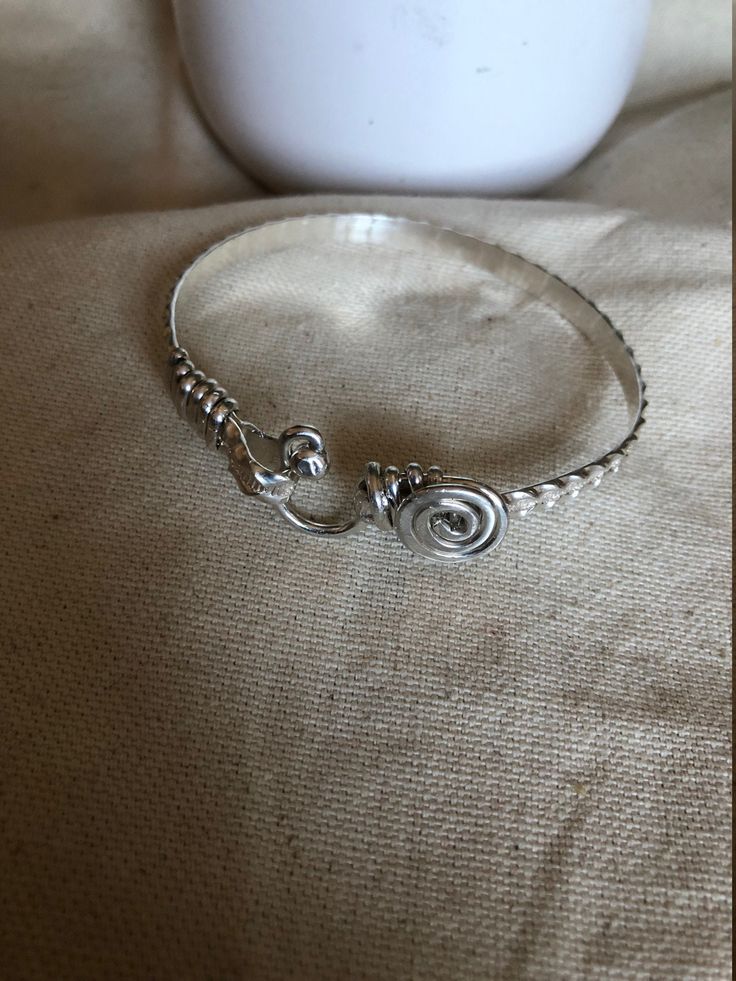 This is a handcrafted bangle/bracelets. It is designed with an oval shape to ensure a proper fit. It is the perfect gift for mothers, sisters, birthdays, daughters, and lovers. This is a simple classy bracelets.  It is  5mm in wide, , handcrafted wire-wrapped bangle bracelet, wire wrapped in sterling silver. A dainty, elegant bracelet that can be used as statement jewelry. As a Caribbean person St.Croix born and raised) these hook-styled bracelets are known to bring good luck or a meaningful ges Artisan Silver Bangle Hand Wrapped, Artisan Hand-wrapped Silver Bangle, Elegant Spiral Hand Wrapped Jewelry, Sterling Silver Hand Forged Bangle As Gift, Hand Forged Sterling Silver Bangle Gift, Artisan Sterling Silver Bangle As Gift, Unique Adjustable Bracelet With Sterling Silver Clasp, Artisan Hand Wrapped Silver Bracelets, Oval Sterling Silver Bangle As Gift