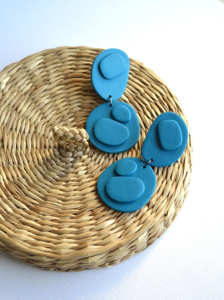 three blue earrings sitting on top of a wicker basket next to a white table