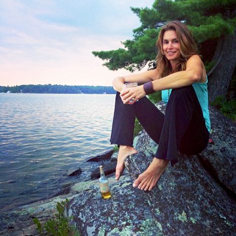 a woman sitting on top of a rock next to a body of water with a drink in her hand