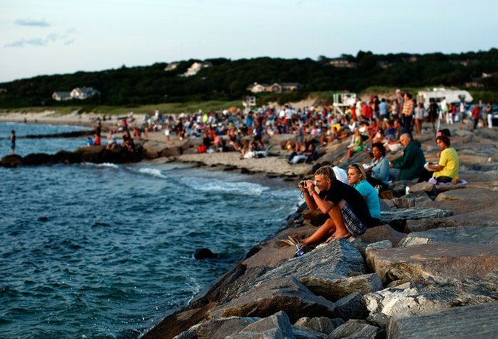 many people are sitting on the rocks by the water