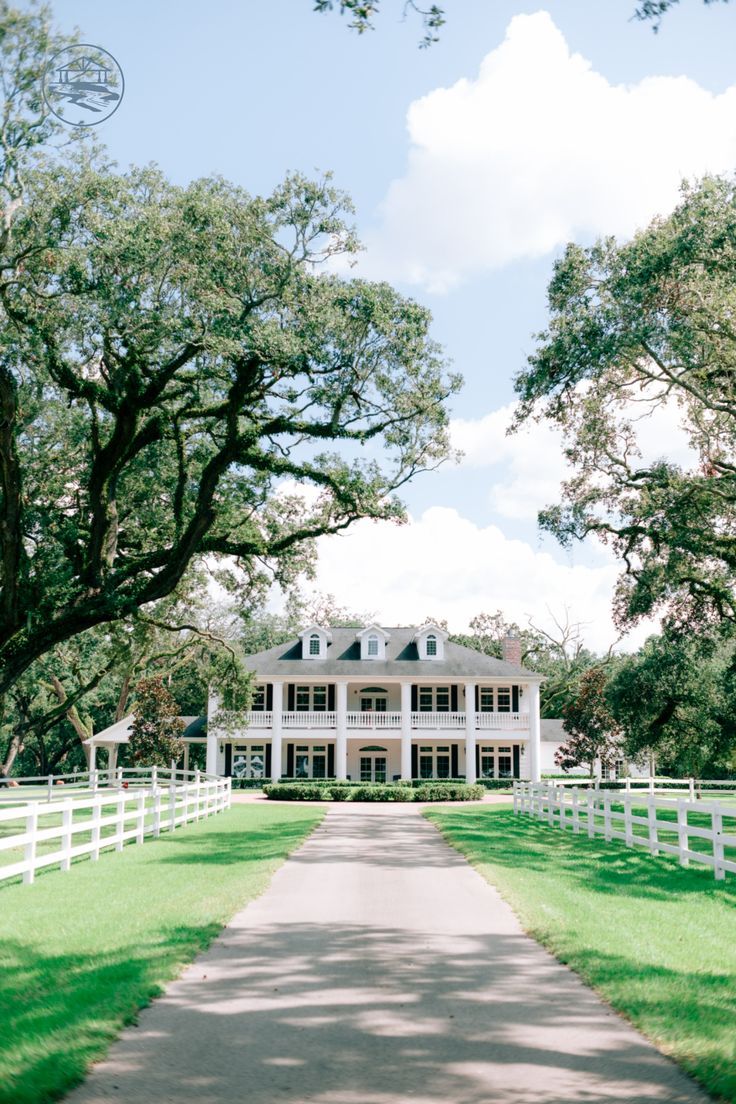 a large white house sitting on top of a lush green field next to a road