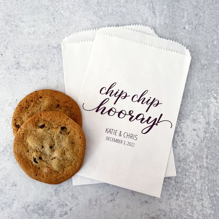 two chocolate chip cookies sitting next to each other on top of a piece of paper