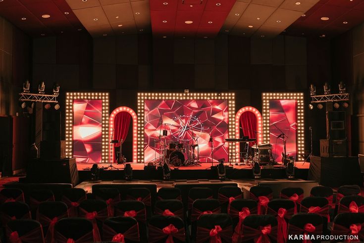 the stage is set up for an event with red lights and curtains on it, along with black chairs