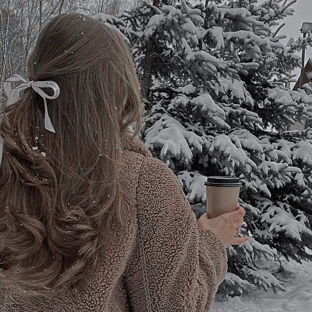 a woman holding a coffee cup in front of snow covered trees