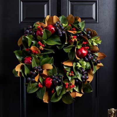 a wreath with berries and leaves hanging on a black front door, surrounded by greenery