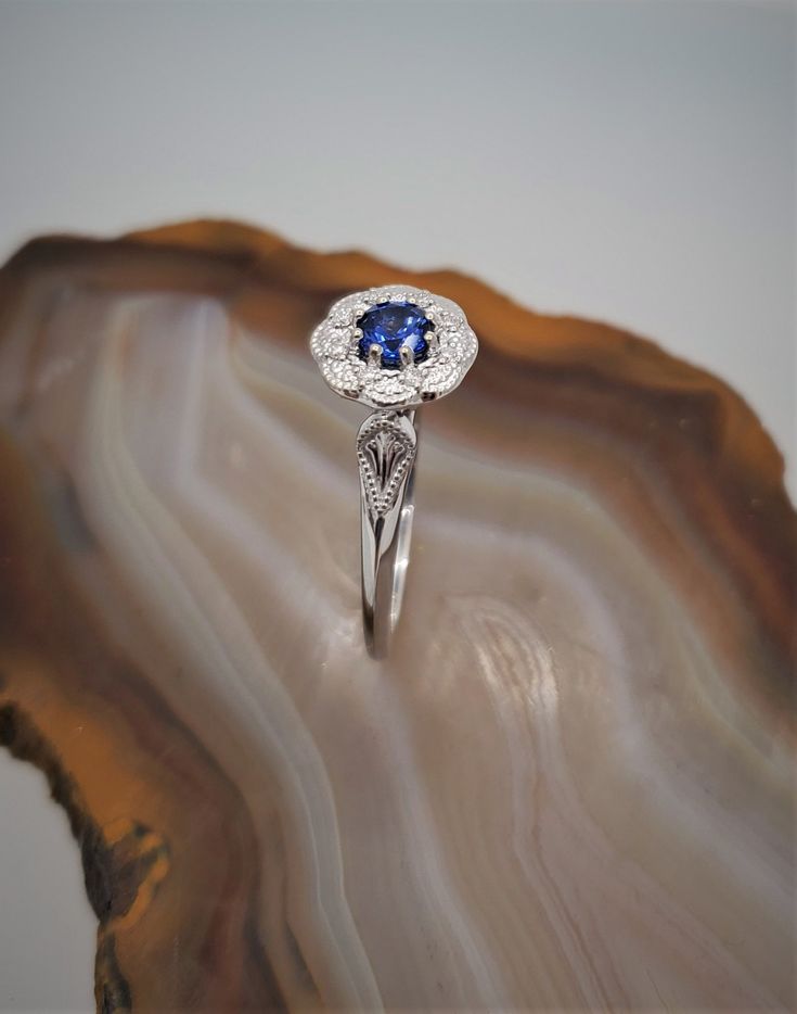 CJ71782SPH Vintage inspired sapphire-diamond 14k gold ring. This is a gorgeous 14k white gold flower halo ring with a migraine design. Eight round diamonds are set around the halo with a beautiful genuine blue sapphire set in the center. Sapphire is .44cts, approximately 4.5mm. Diamonds are .06cts in total weight. Halo measures approximately 9mm. Currently the ring is size 7 but can be resized, please inquire. Diamond White Diamond Ring With Sapphire Halo Setting, Sapphire Diamond Ring With Halo Setting For Promise, Sapphire Diamond Cluster Ring With Halo Design, Sapphire Halo Ring In 14k White Gold, Sapphire Cluster Ring With Halo Setting For Promise, Classic 14k White Gold Sapphire Ring With Halo Setting, Wedding 14k White Gold Sapphire Ring With Halo Design, Sapphire Diamond Ring With Halo Setting For Anniversary, White Gold Sapphire Ring With Diamond Halo Design