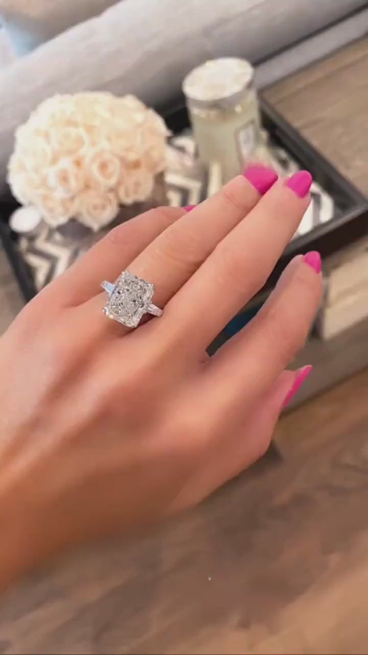 a woman's hand with a ring on her finger and flowers in the background