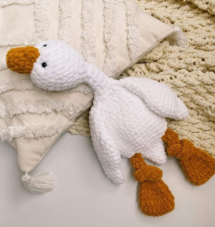 a white stuffed duck laying on top of a pillow next to a knitted blanket