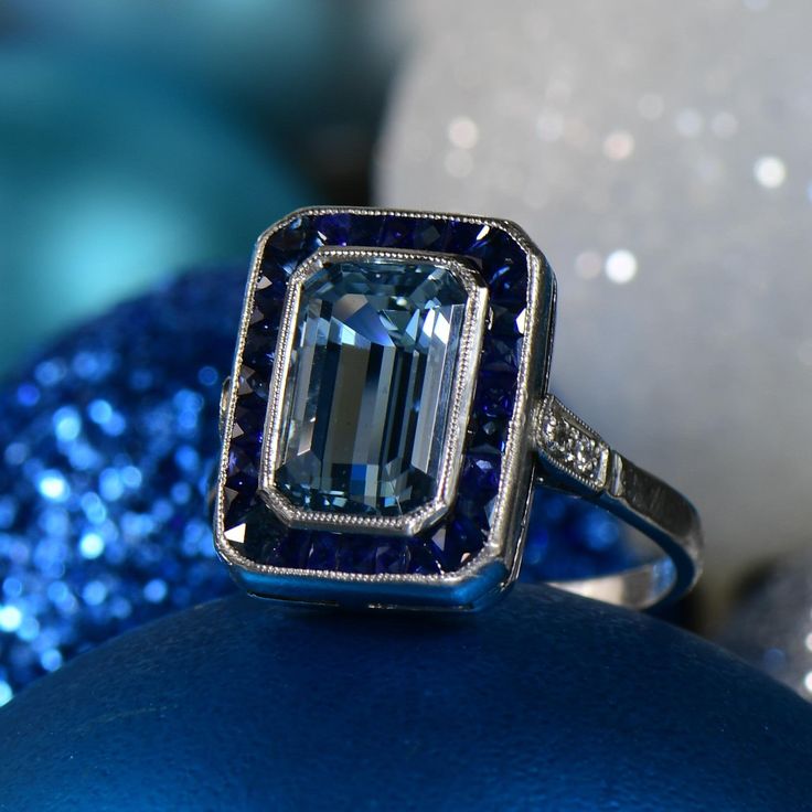 an emerald colored diamond ring sitting on top of a blue ornament