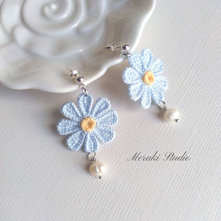 a pair of blue and white flower earrings with pearls on the end, sitting next to a seashell