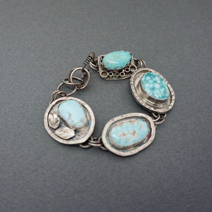 This lovely gemstone bracelet is one of a kind and a great statement piece!  Each charm link has been embellished in a very unique way to make a one of a kind bracelet. The lovely turquoise stones  are of the highest quality. I have used 2 Cloud Mine Turquoise stones with 2 Sleeping Beauty Stones. The turquoise contrasts beautifully with the oxidized sterling silver. I have added a variety of embellishments to the outside of the stones and then finished the bracelet with a handcrafted hook clasp. The bracelet is about 7" and is somewhat adjustable.  The bracelet will be sent in a linen bag, inside a gift box, ready for gift giving! *Take a closer look* 4 turquoise cabochons- Cloud Mine and Sleeping Beauty hook clasp Length-7" adjustable *Surface Features* Granulation Square wire oxidation Unique Turquoise Sterling Silver Bracelets, Handmade Turquoise Sterling Silver Bracelets, Unique Turquoise Metal Bracelet, Handmade Turquoise Bracelet Jewelry, Handmade Turquoise Bracelet, Sterling Silver Jewelry With Turquoise, Unique Turquoise Bracelet Jewelry, Turquoise Metal Bracelet Jewelry, Artisan Turquoise Gemstone Bracelet