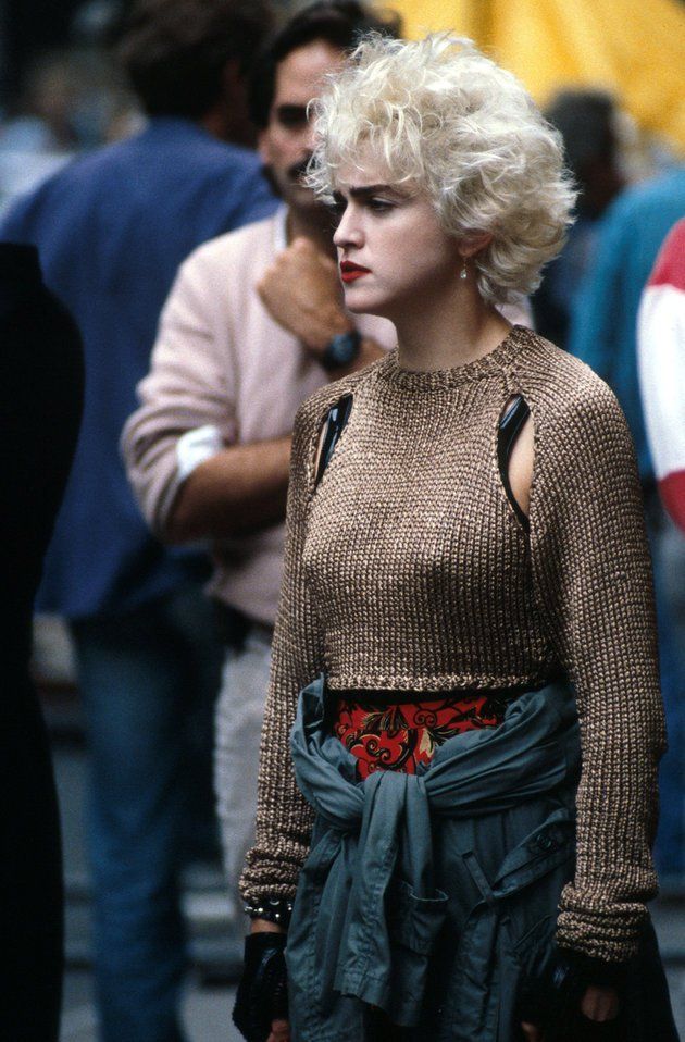 a woman with blonde hair wearing a brown sweater and green skirt standing on the street