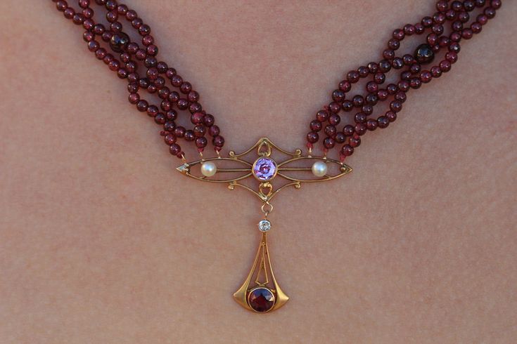 "This royal garnet necklace is a perfect example of how stunning the Art Nouveau period is. It is a wonderful pairing of clean simple lines with flowing forms and gemstones adding a lovely accent. In this piece, hand woven garnet beads are paired with the 14k yellow gold showpiece containing two pearls, a pink sapphire, and diamond. The clasp is just as elegant with filigree and diamonds. THE DETAILS: Length: 19\" (483mm) Length of centerpiece: 1.37\" (35mm) Width at beaded section: .47\" (12mm) Elegant Ruby Briolette Necklace, Elegant Ruby Round Beads Jewelry, Elegant Ruby Necklace With Polished Beads, Elegant Ruby Jewelry With Gemstone Beads, Elegant Amethyst Gemstone Bead Necklaces, Elegant Amethyst Gemstone Beads Necklace, Elegant Amethyst Round Bead Necklaces, Elegant Necklaces With Round Amethyst Beads, Elegant Amethyst Necklaces With Round Beads