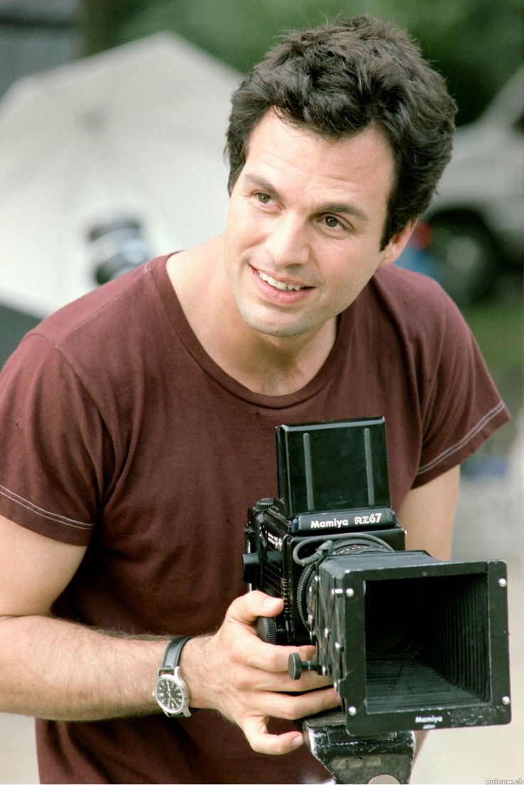 a man holding an old fashioned camera in his right hand and smiling at the camera