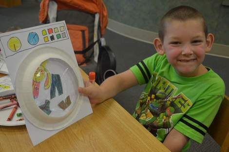 a young boy sitting at a table with paper plates and crayons