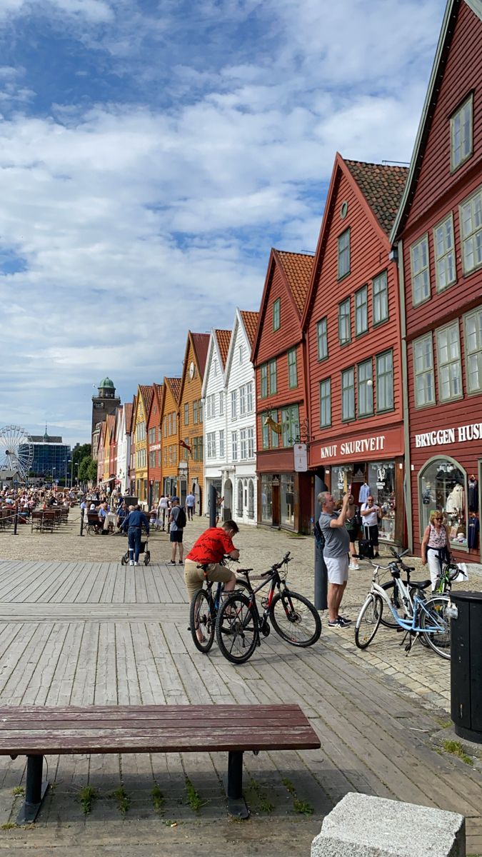 people are walking and riding bikes on the boardwalk in front of red buildings with white trim