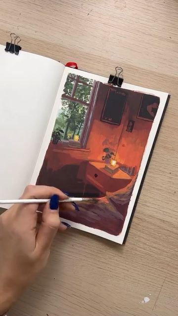 a person is holding a pen and drawing in an open photo book on a wooden table