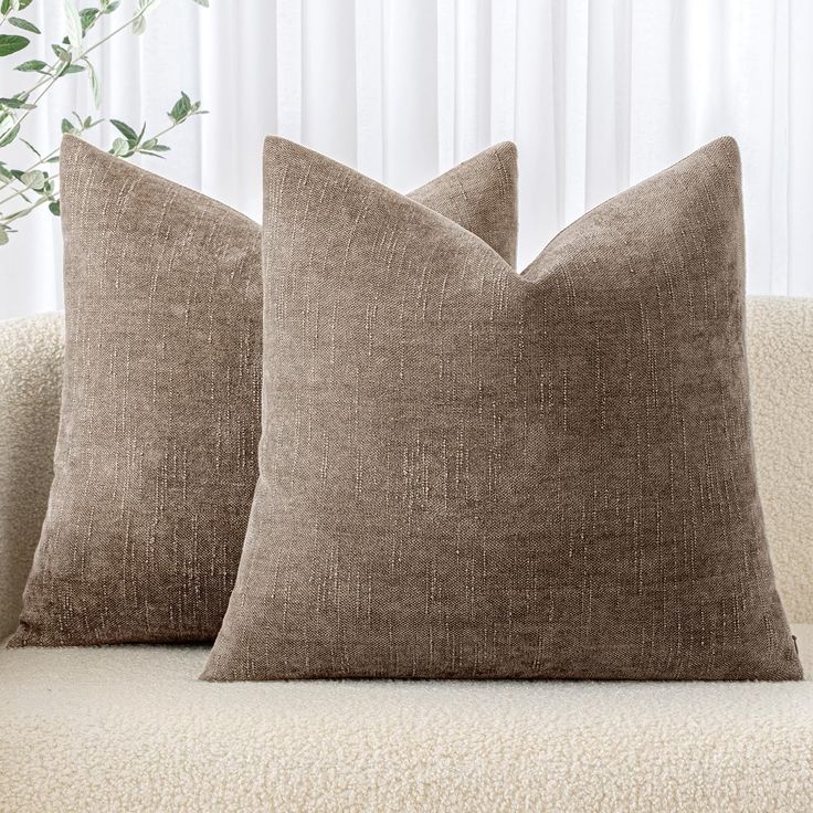 two brown pillows sitting on top of a couch next to a potted green plant