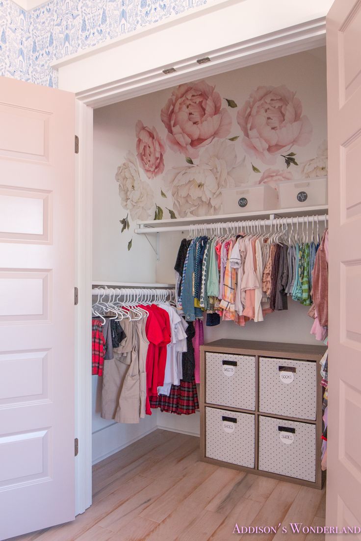 an open closet with clothes hanging on the wall and flowers painted on the wall behind it