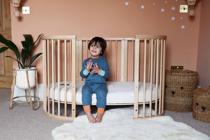 a young child sitting in a wooden crib next to a white sheepskin rug