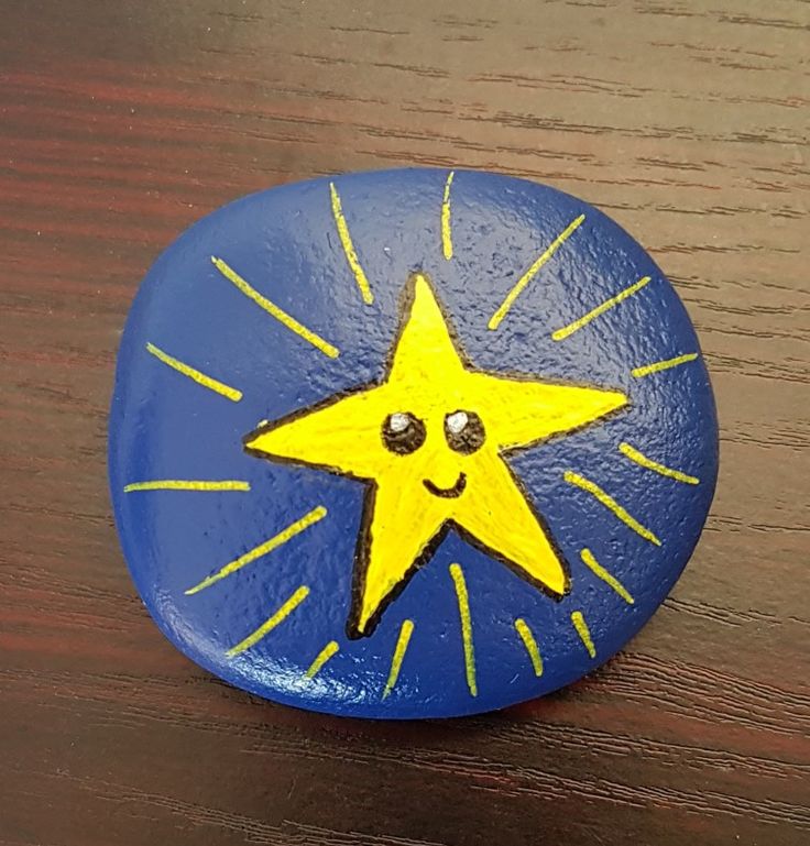 a blue and yellow painted rock with a smiling star on it's face, sitting on a wooden table