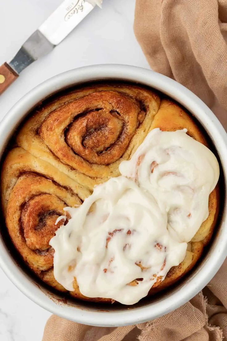 cinnamon rolls with icing in a white bowl on a table next to a knife