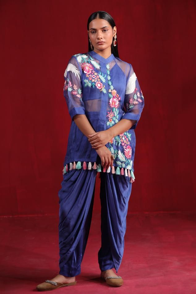 Blue organza shirt style kurta with all over floral pattern, multi color thread and bead embroidery. Paired with pleated draped dhoti pant and halter V neck corset style blouse.
Components: 3
Pattern: Hand Embroidered
Type Of Work: Thread and Bead Work
Neckline: Kurta: Band Collar, Blouse: Halter Neck
Sleeve Type: Kurta: Three Quarter Sleeves, Blouse: Sleeveless
Fabric: Kurta: Organza, Blouse and Dhoti: Satin Silk
Color: Blue
Other Details: 
Fringe drop tasselled kurta hem
Round back
Model heigh Blue Resham Embroidery Pant Set For Wedding, Blue Wedding Pant Set With Resham Embroidery, Traditional Blue Pant Set With Zari Work, Bollywood Pant Set With Resham Embroidery And Traditional Drape, Traditional Indigo Sets With Dupatta, Blue Resham Embroidered Pant Set For Wedding, Traditional Blue Palazzo Set With Floral Embroidery, Indigo Sets With Dupatta For Navratri, Navratri Traditional Drape Pant Set With Dupatta