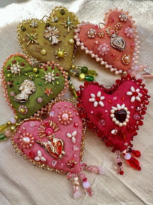 four heart shaped brooches are laying on a white cloth covered table with beads