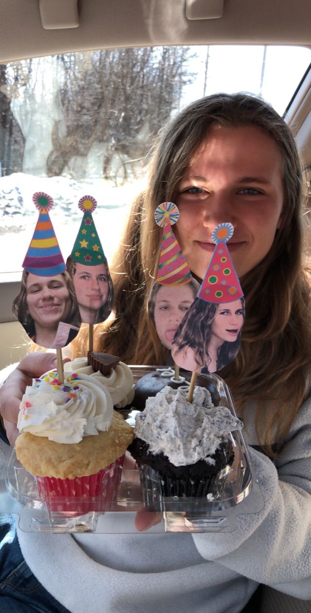 a woman is holding up cupcakes with candles on them in the back seat of a car