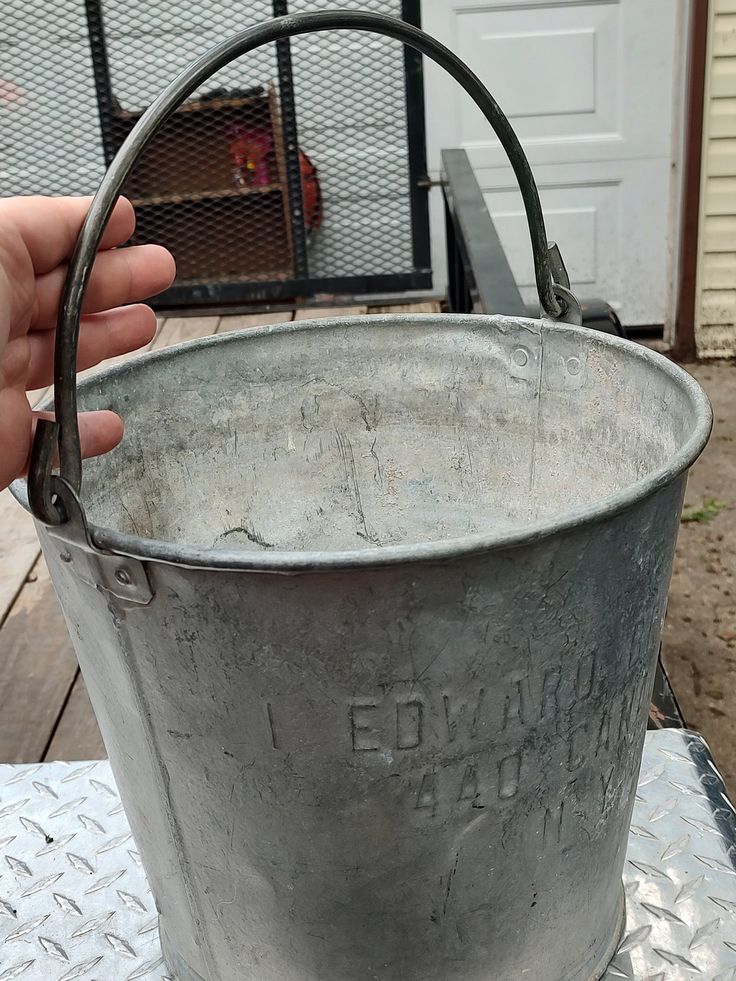 a hand holding a metal bucket on top of a table