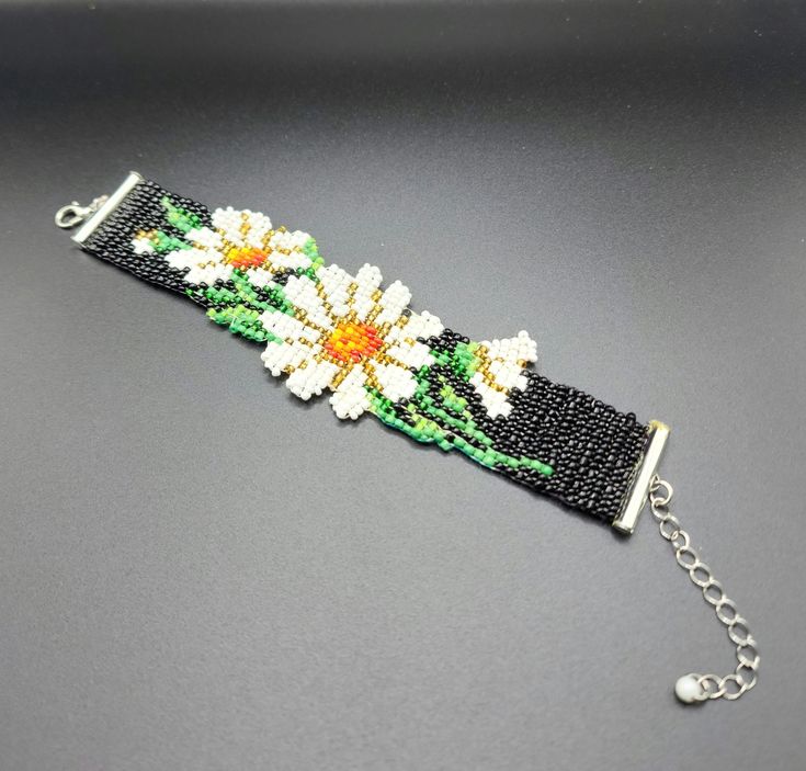 the beaded bracelet is decorated with flowers and beads on a black background, along with a silver chain