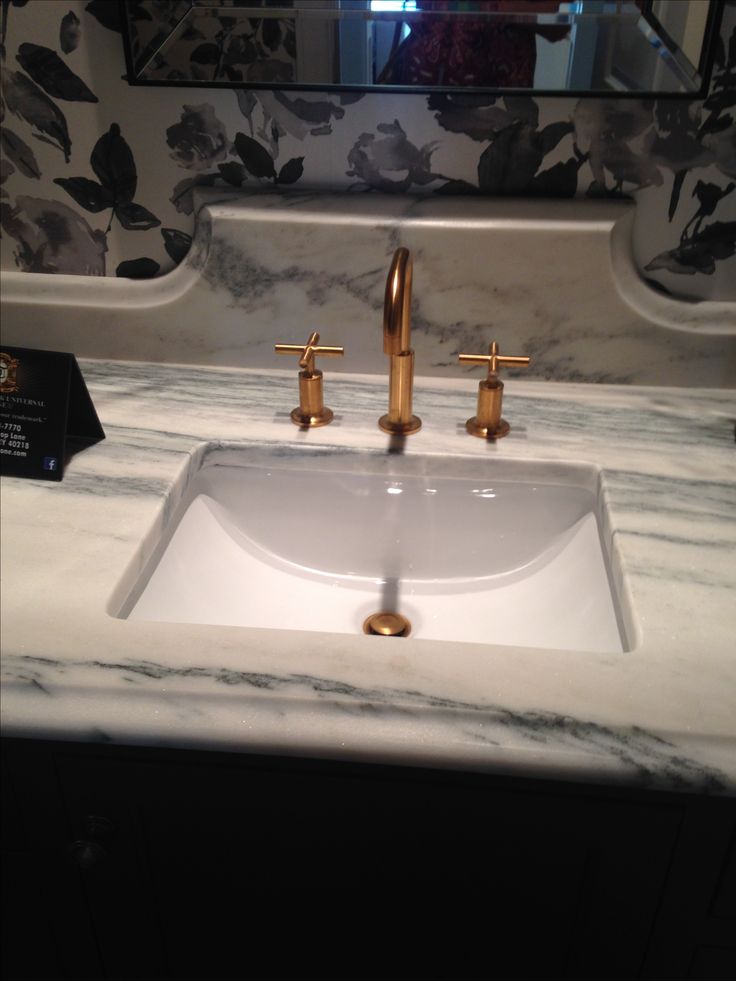 a bathroom sink with two faucets and a marble counter top in front of a mirror