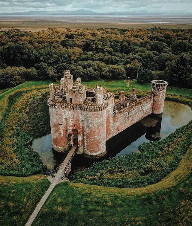 an aerial view of a castle in the middle of a green field with trees around it