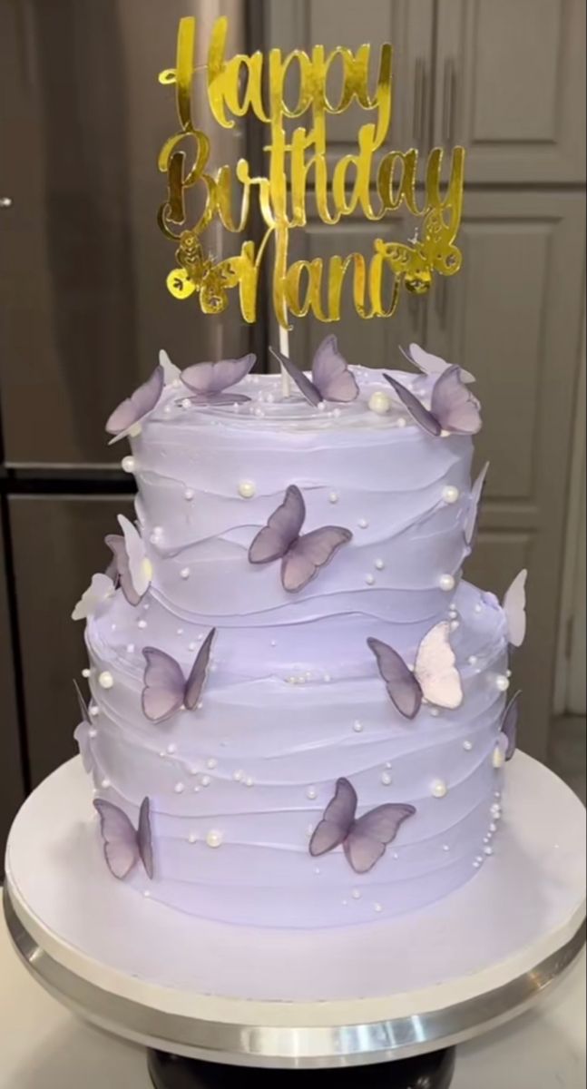 a three tiered cake with purple icing and butterflies on top, sitting on a table