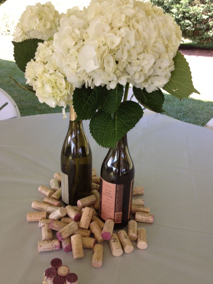 two wine bottles with corks and flowers in them sitting on a table next to each other