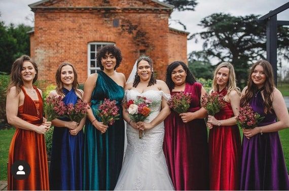 a group of women standing next to each other in front of a brick building holding bouquets