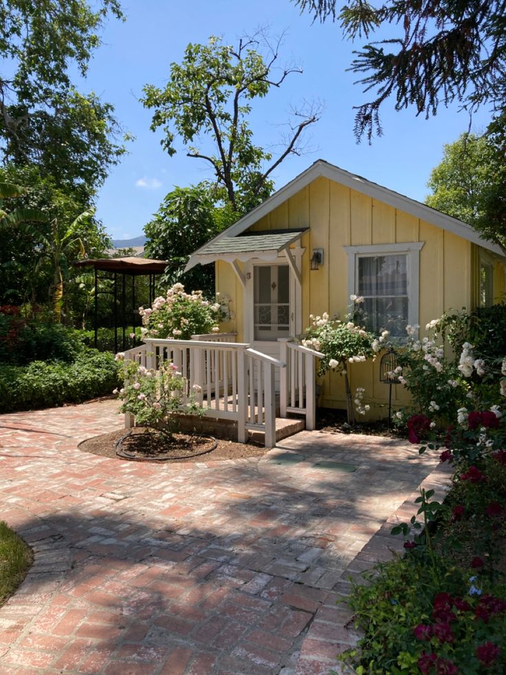 a small yellow house surrounded by trees and flowers