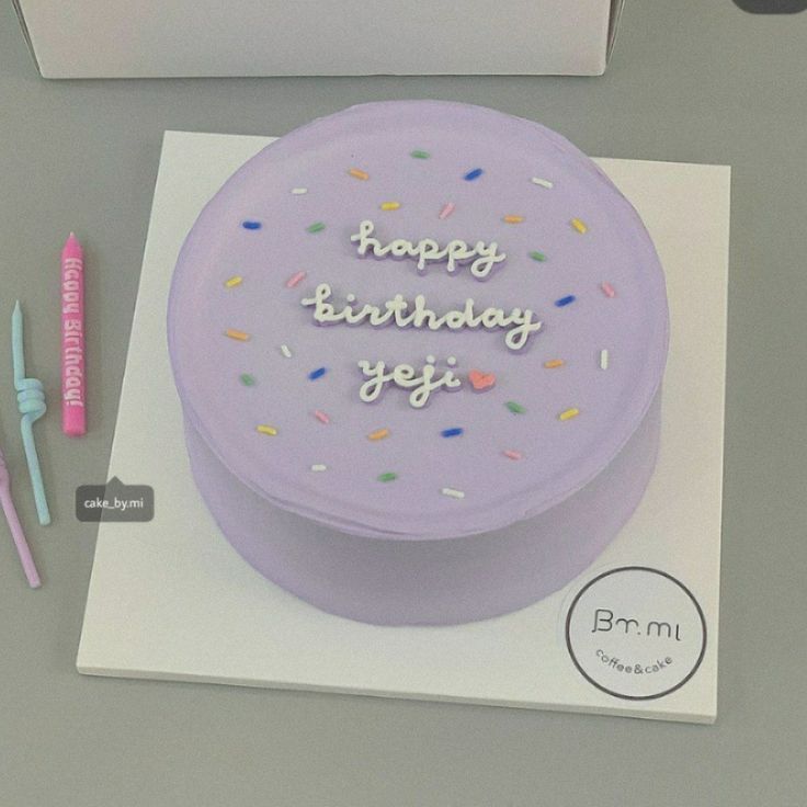 a purple birthday cake sitting on top of a white box next to two toothbrushes