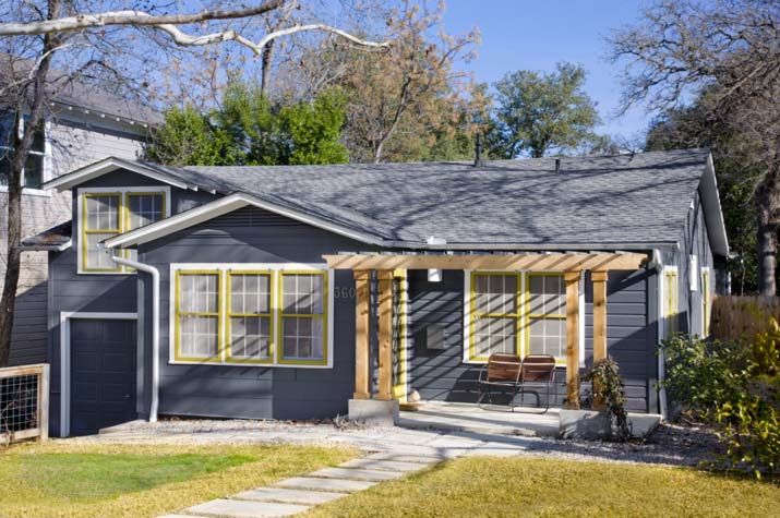 a small gray house with yellow windows and a wooden pergolated walkway leading to the front door