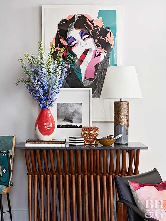 a vase with flowers on top of a wooden table next to a lamp and pictures