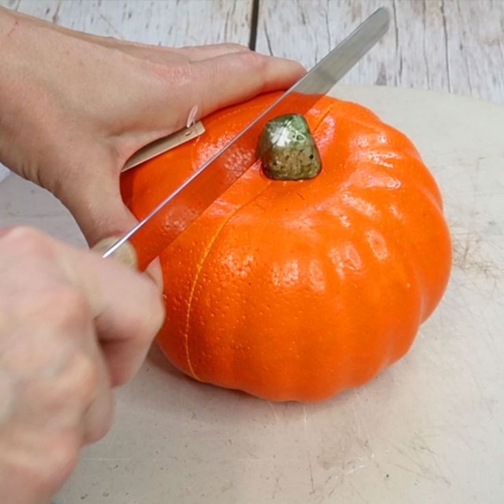 someone cutting up a pumpkin with a pair of scissors on the top of it